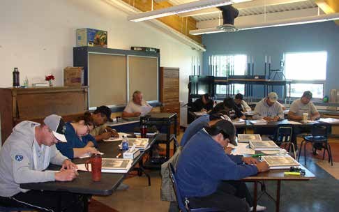 Participants seated at tables in a classroom working through printed course material.