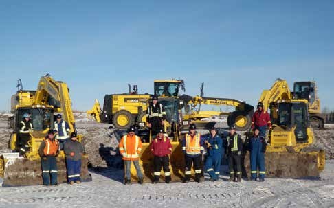 A crew in high-visibility vests standing in front of a line of excavators and heavy equipment at a worksite.